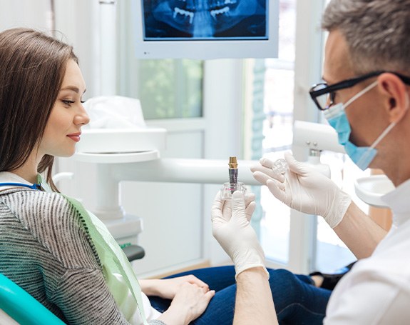 Dentist showing woman sample dental implant